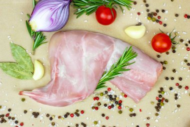 Çiğ, pembe tavşan bacağı eti, yeşil biberiye ve hafif ahşap kesim tahtası arka planında taze sebzeler..