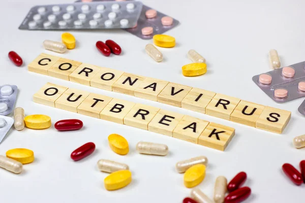 The medical phrase coronavirus outbreak with pills, capsules and tablets on light background. Epidemic alert concept.