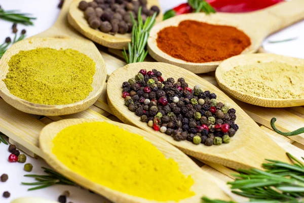 Variety of spices and seasonings (indian curry, different pepper, paprika powder, salt, dry ginger and curcuma) for cooking in wooden spoons on white kitchen table background.