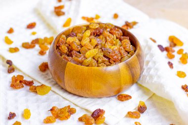 Kahverengi üzümler (kurutulmuş sarı üzüm) açık arkaplanda yuvarlak ahşap kase içinde.