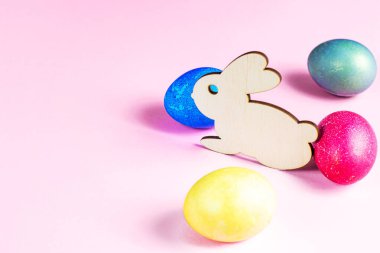 Renkli yumurtaları olan komik ahşap Paskalya Tavşanı açık pembe arka planda fotokopi alanı olan bir bayramı simgeliyor..