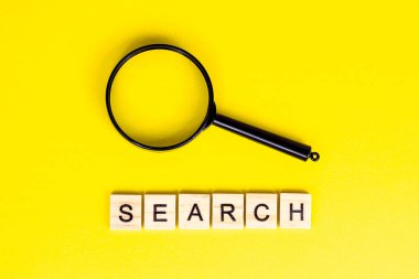 Açık sarı arkaplanda arama sözcüğüyle siyah büyüteçin üst görünümü.