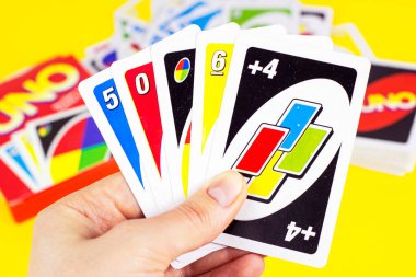 MINSK, BELARUS - 30 Mart 2021: Masa keyfi aile oyunu Uno, oyuncunun elinde parlak sarı arka planda kağıt oynuyor.