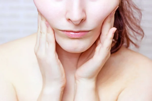 Young caucasian woman touching her face with hands doing face fitness exercises. Facial lifting and massage concept.