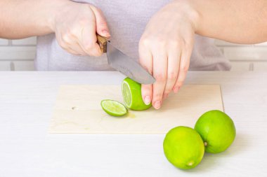 Taze yeşil ekşi kireç, bıçakla kesilmiş açık ahşap kesme tahtası, kadın eli mutfakta..