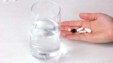 Beyaz kadın elleri elinde farklı ilaçlar (haplar ve kapsüller) ve hafif ahşap arka planda bir bardak su ile