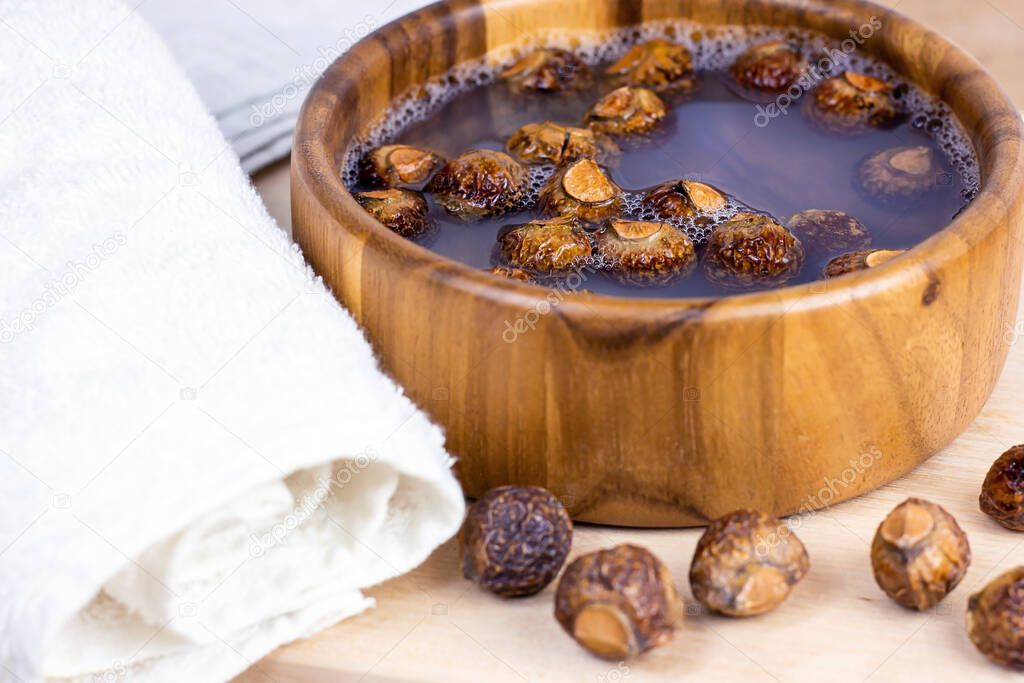 Brown dry soap nuts (Soapberries, Sapindus Mukorossi) in the water with the towel for organic laundry and gentle natural skin care on light background.