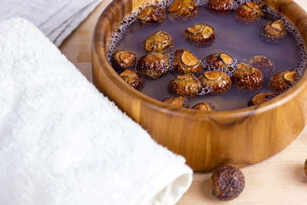 Brown dry soap nuts (Soapberries, Sapindus Mukorossi) in the water with the towel for organic laundry and gentle natural skin care on light background.