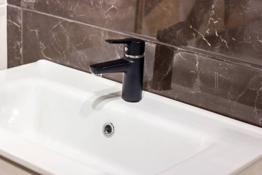 Yeni modern siyah su musluğu. Banyoda seramik duvarda beyaz lavabo var..