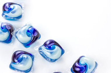 Makine için sıvı deterjan içeren parlak mavi çamaşır kapsülleri ve kapsülleri beyaz giysi arka planında fotokopi alanı ile.