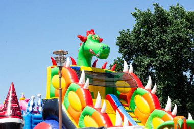 LIDA, BELARUS - 10 HAZİRAN 2021 Yazın eğlence parkında çocuklar için parlak renkli lastik kaydırak ve trambolin cazibesi.