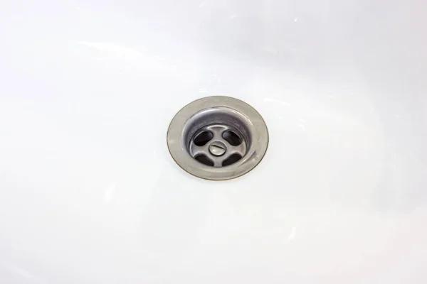 Metallic water drain hole in the white ceramic sink in the bathroom close up.