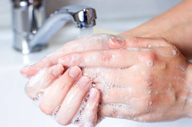 Genç beyaz kadın banyoda su ve sabun köpüğüyle ellerini yıkıyor..