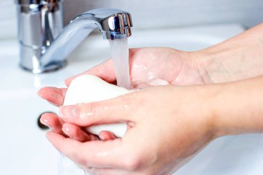 Genç beyaz kadın banyoda su ve sabunla ellerini yıkıyor..