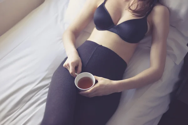 ベッドの上でお茶を飲んで下着姿で若い女性 — ストック写真