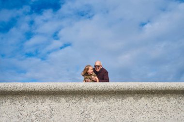 Yazın bir anaokulu öğrencisi dedesiyle birlikte duvarda dinleniyor.