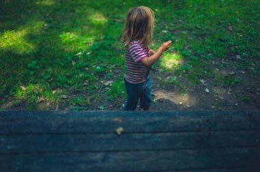 Küçük bir anaokulu öğrencisi ormanda bir piknik masasının yanında duruyor.