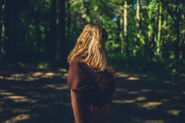 Yavrusu askıda olan genç bir anne ormanda duruyor.