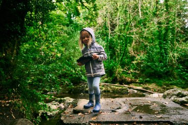 Küçük bir anaokulu öğrencisi büyük bir kömür parçasıyla ormanda dikiliyor.
