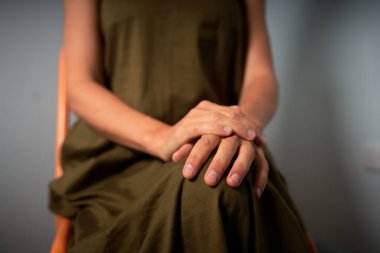 Genç bir kadın, elleri dizlerinin üzerinde bir sandalyede oturuyor.