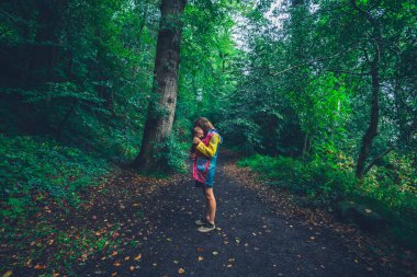 Genç bir anne, bebeği askıda ormanda yürüyor.