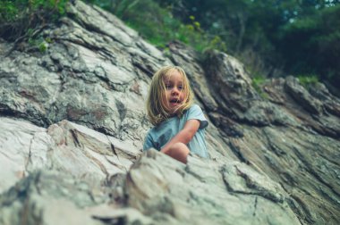 Küçük bir anaokulu öğrencisi sahilde kayalara tırmanıyor.