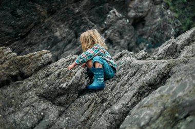 Küçük bir anaokulu öğrencisi sonbaharda kayalara tırmanıyor.