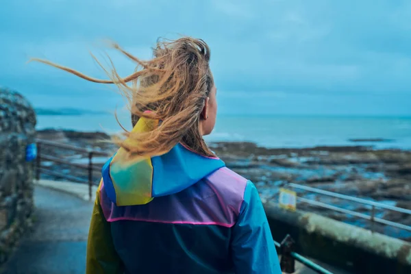 レインコートを着た若い女性が海辺に立っている — ストック写真