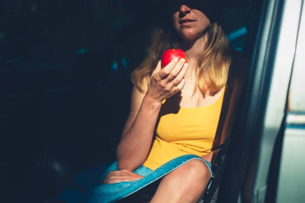 A young woman is sitting in a car eating an apple