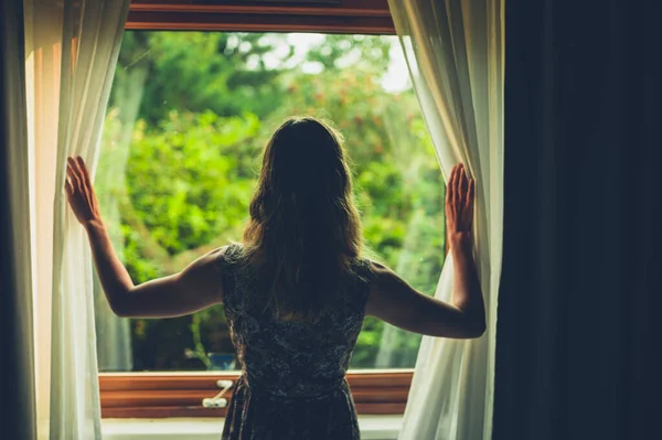 若い女性が朝起きてカーテンを開けて外を見ている — ストック写真