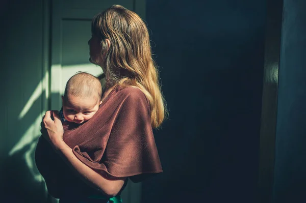 물매에 아기를 어머니 실내에서 햇빛을 받으며 — 스톡 사진