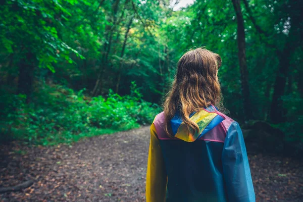 レインコートを着た若い女性が秋に森の中を歩いている — ストック写真