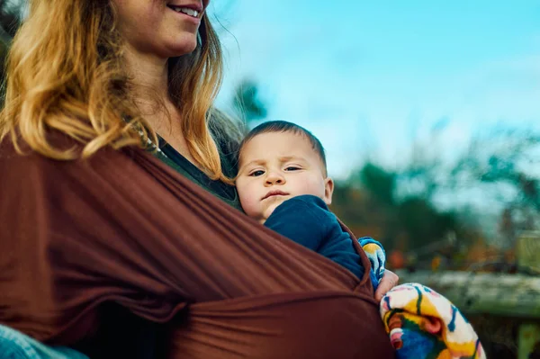 若い母親は秋の日にスリングで赤ちゃんと森の中にいます — ストック写真