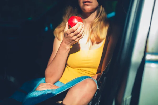 若い女性がリンゴを食べて車の中に座っている — ストック写真