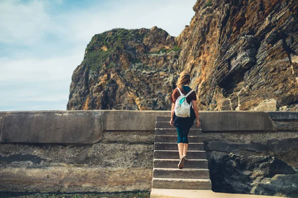 A young woman is climbing some steps on the coast by some rocks