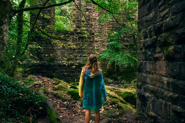 Genç bir kadın ormanda taş bir duvarın yanında yürüyor.