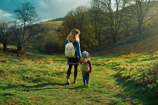 幼い母親が秋の日に幼稚園のある草原や森を歩いている — ストック写真