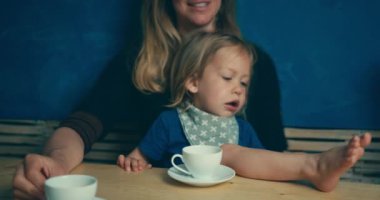 Anne ve küçük oğlu evde çay içiyor.