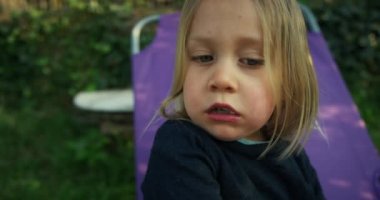 Küçük çocuk dışarıda karyolada otururken yemek yiyor.