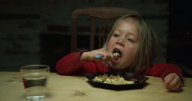 Küçük çocuk masada yemek yiyor.