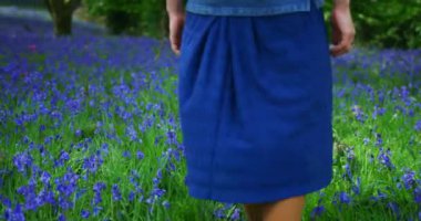 Mor çiçeklerle yeşil alanda yürüyen genç bir kadın.