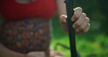 Hamile bir kadın çimlerin üzerinde çim biçme makinesi monte ediyor.