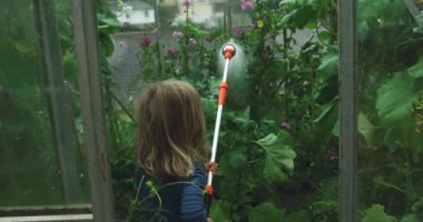 Bahçede çiçekleri sulayan tatlı çocuk.