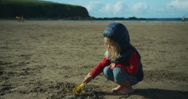 Küçük çocuk kumsalda kumla oynuyor.