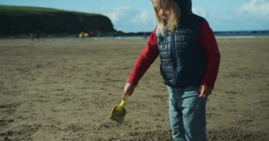 Küçük çocuk kumsalda kumla oynuyor.