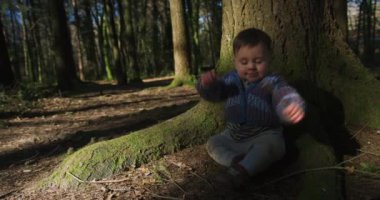 Yerde oturup bahar ormanlarında oynayan sevimli küçük bir çocuk.