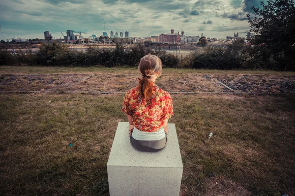 Jonge vrouw buiten zitten en kijken naar stad — Stockfoto