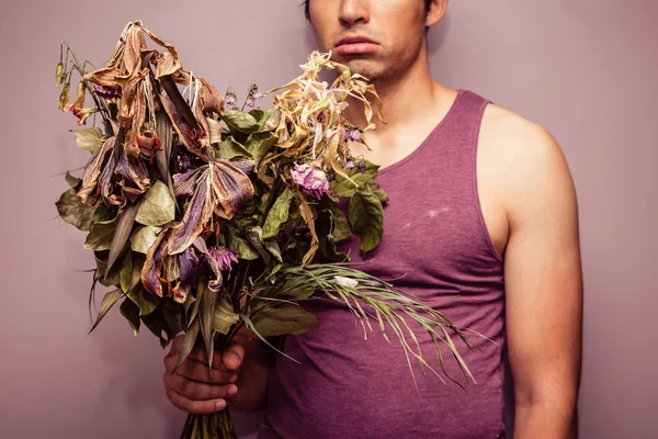 Young man holding bouquet of dead flowers — Stock Photo, Image