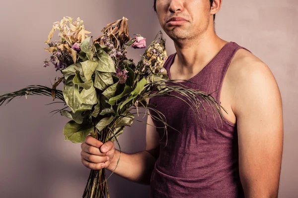 Young man holding bouquet of dead flowers — Stock Photo, Image