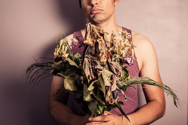 Young man holding bouquet of dead flowers — Stock Photo, Image